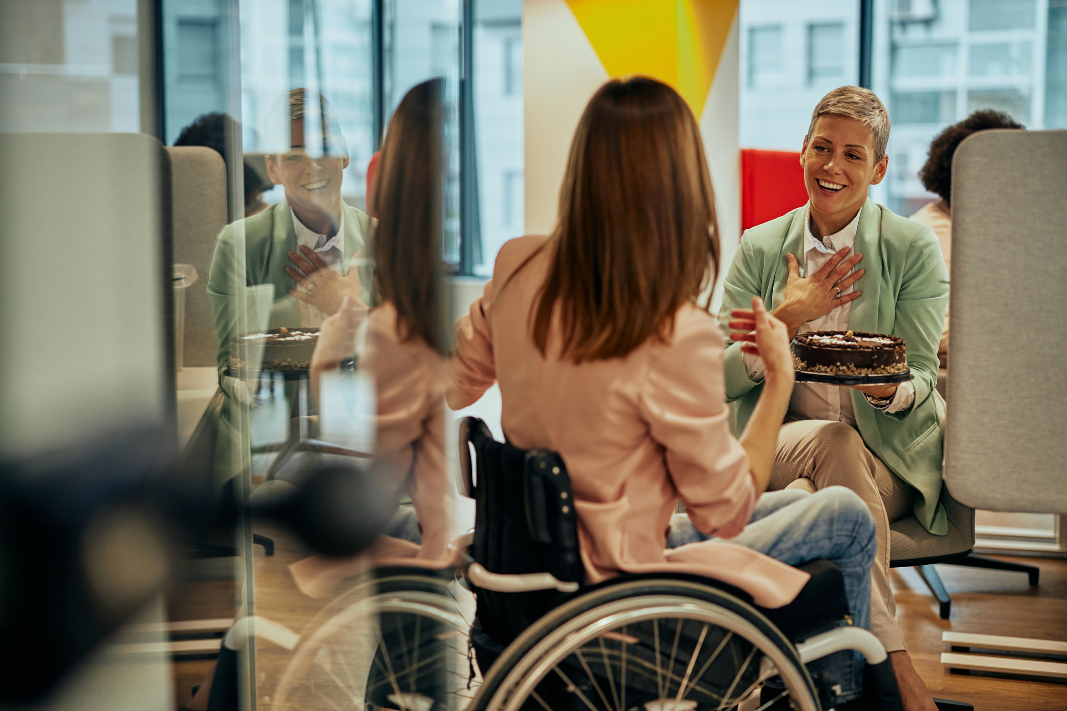 Woman in wheelchair celebrating another woman's birthday at the office.
