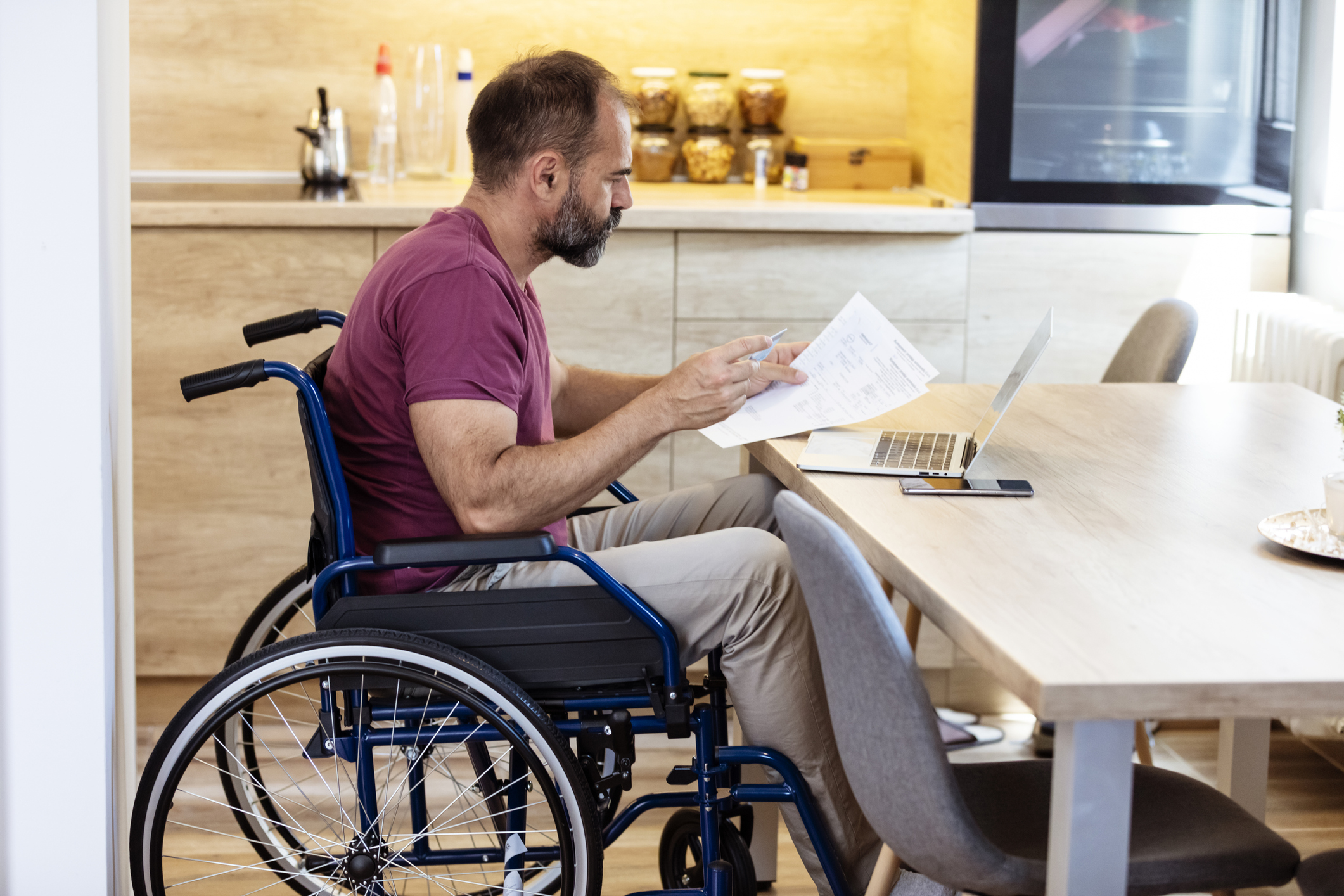 Man in wheelchair looking at paperwork while at his kitchen table.