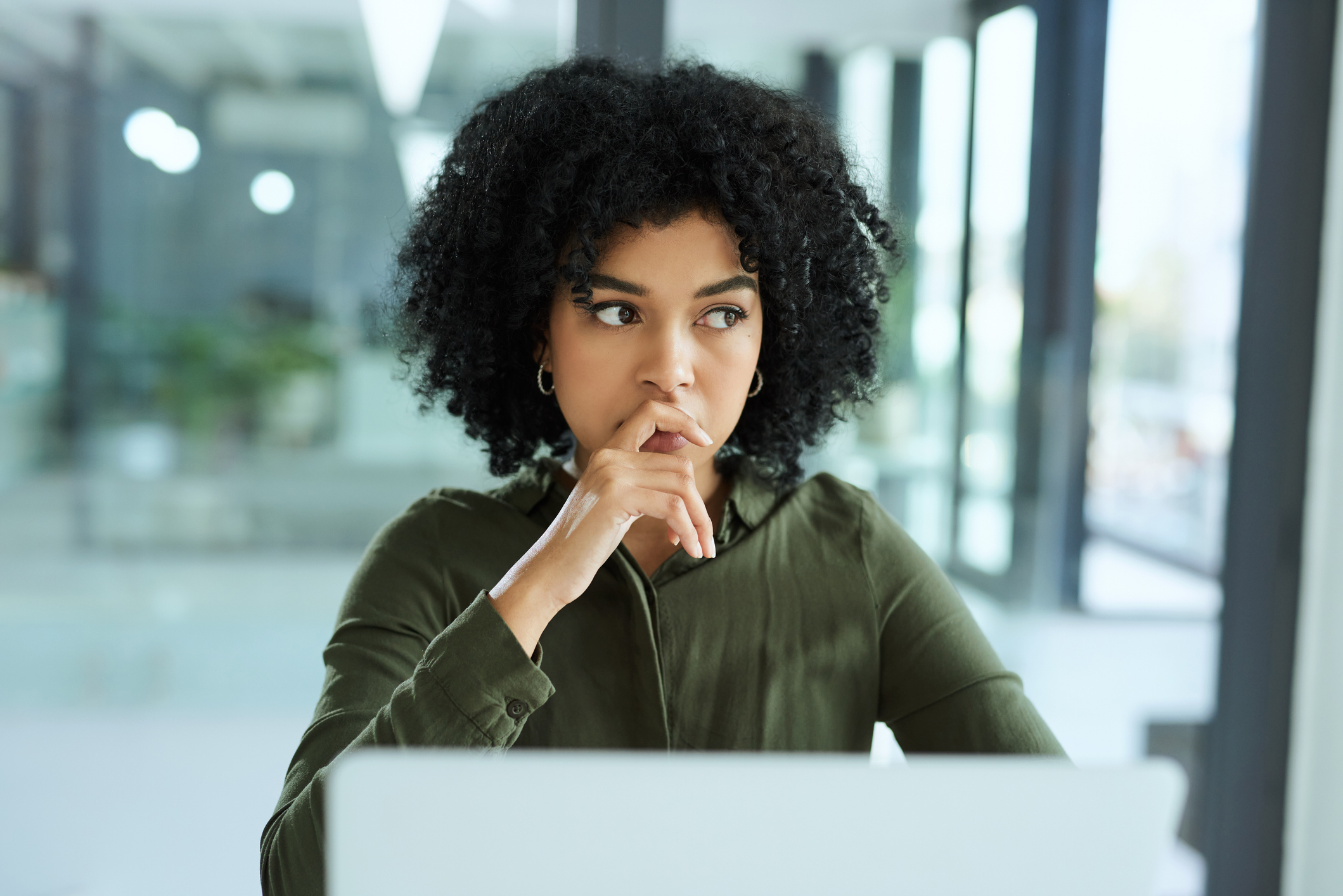 Woman at work at desk in front of laptop, looking out a window while thinking