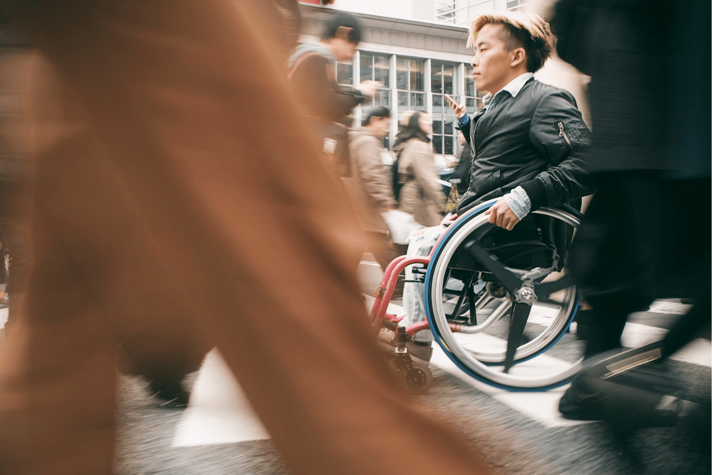 Man in wheelchair moves across a busy, crowded crosswalk.