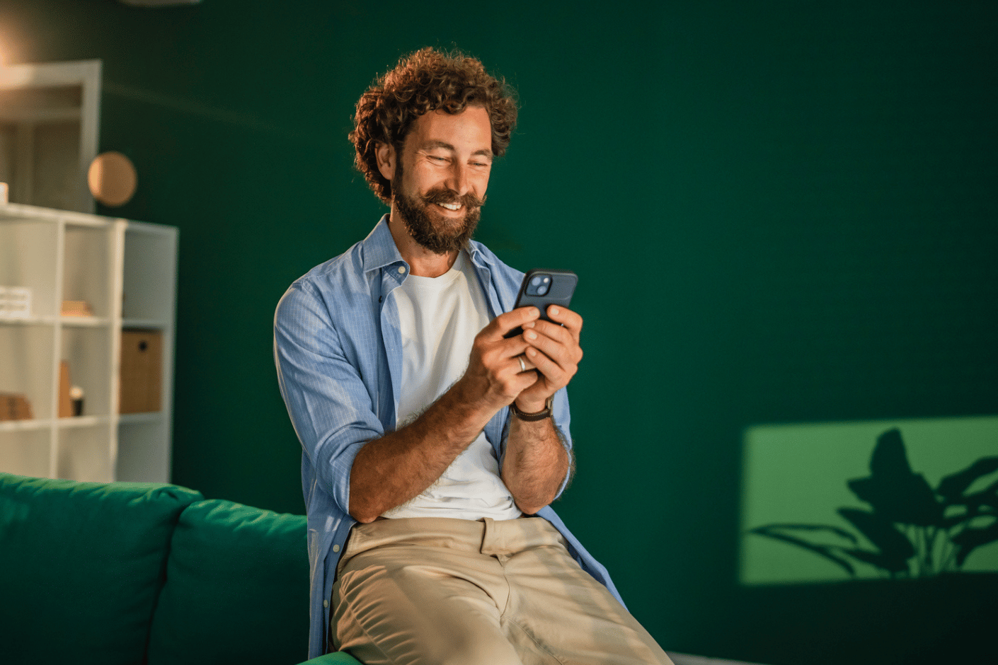 Middle-aged man in living room leaning against a couch while reading his smartphone.