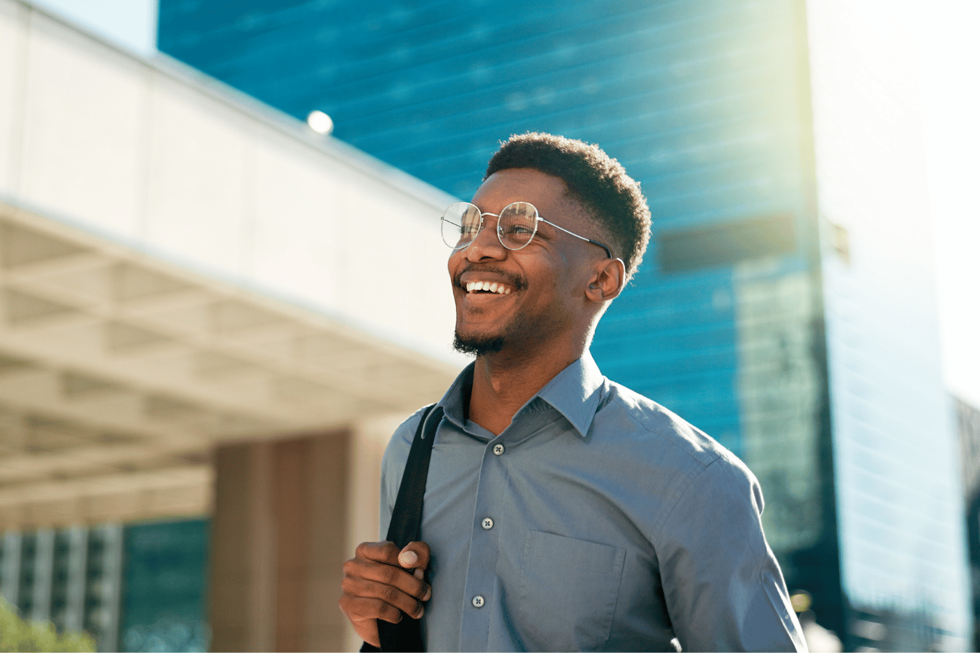 Man walking to work on a city sidewalk, smiling up at the sky.