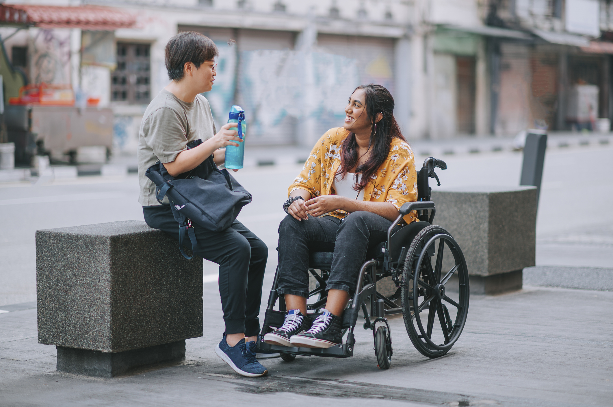 Two people talking outdoors, one seated in a wheelchair.