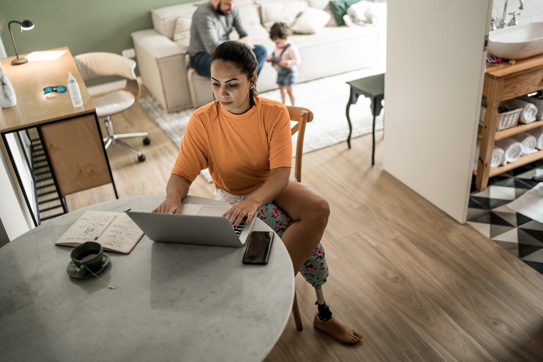 Female amputee working at a computer with a man and child in the background.