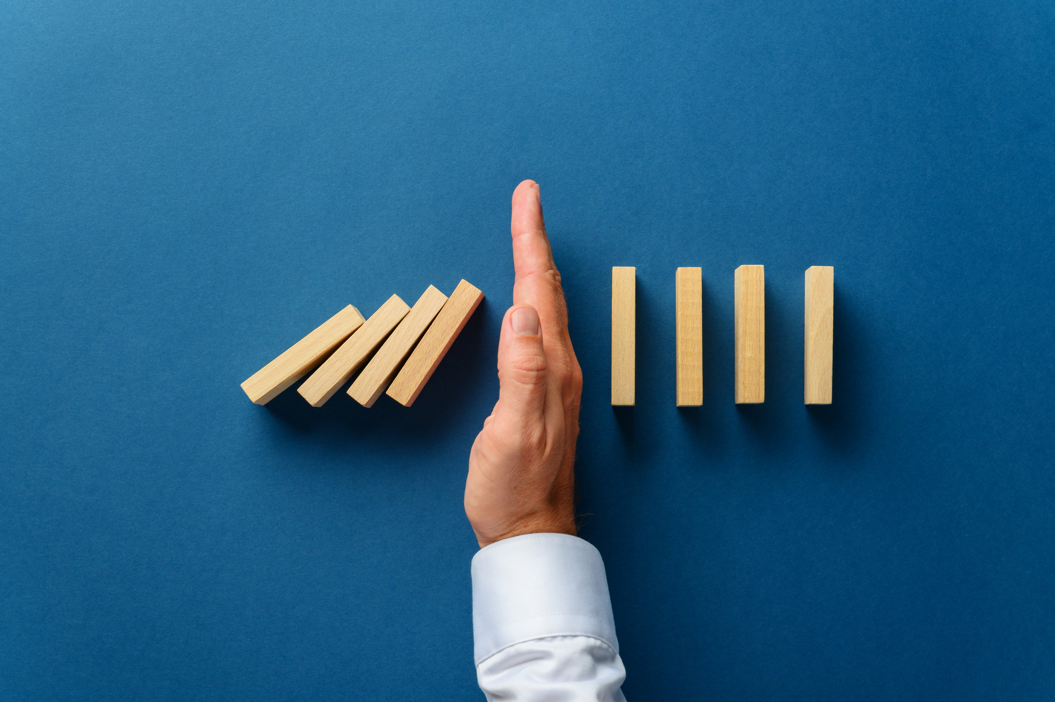 A hand stopping the progression of dominoes falling in line.