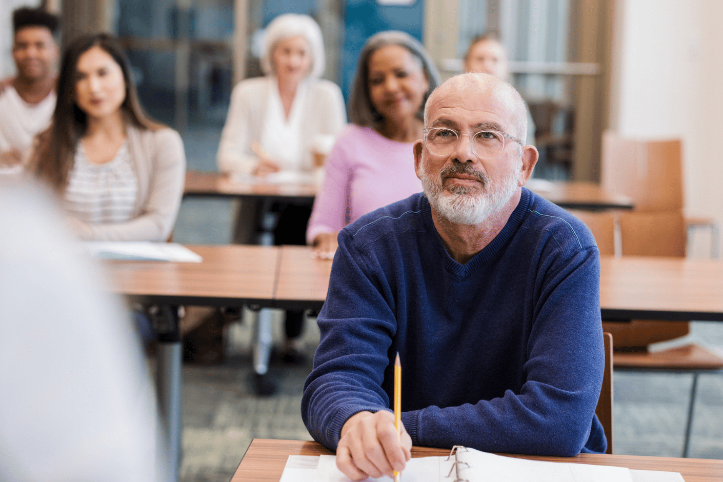Middle-aged male student sits at desk in a training room, listening attentively to the instructor.