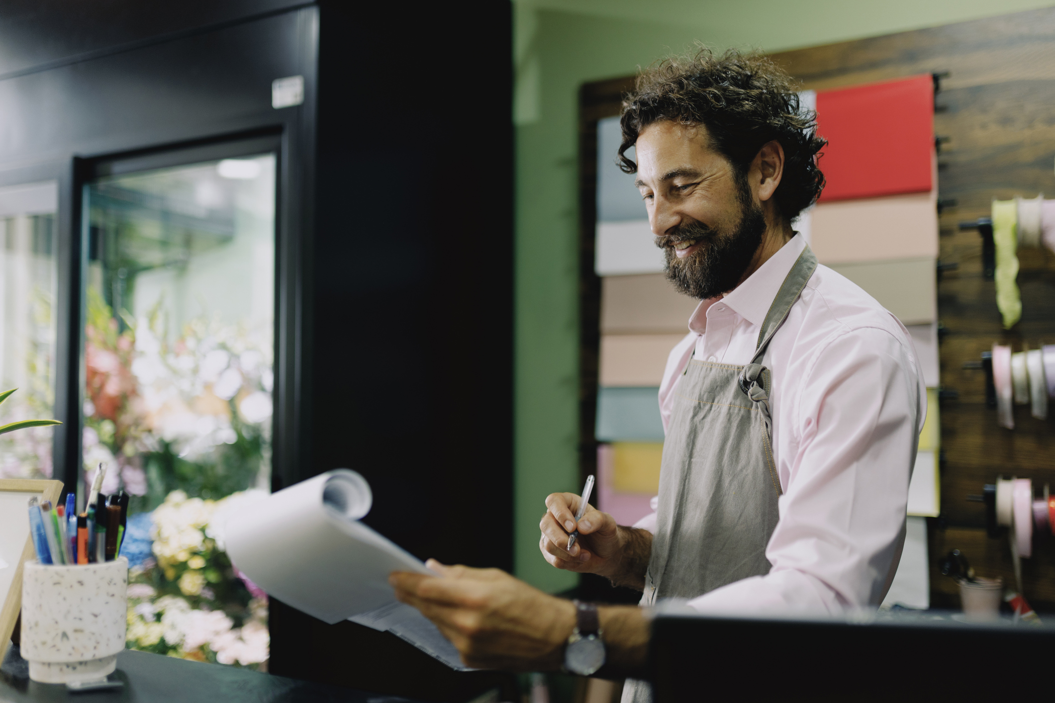 A cheerful middle-aged man working in a florist shop reviews some paperwork.